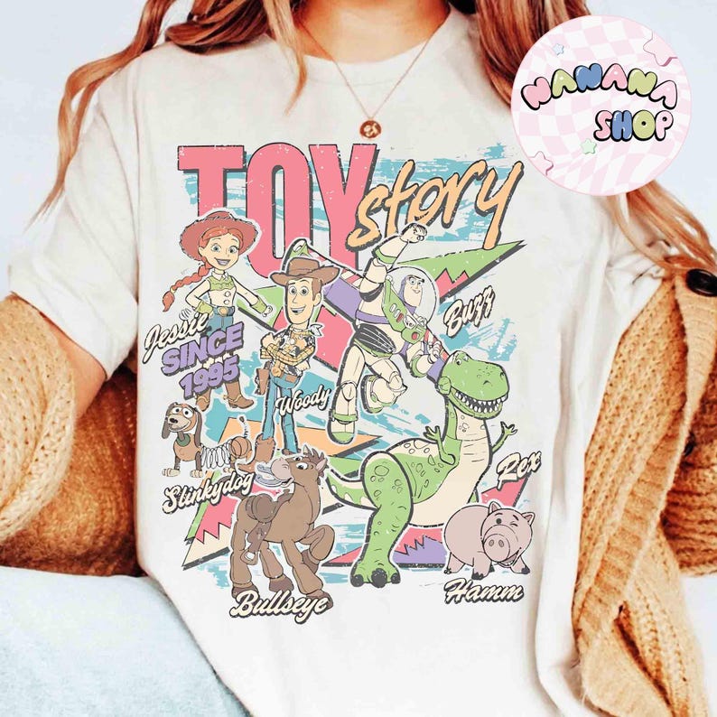Puede incluir: Camiseta color crema con un gr&aacute;fico colorido de los personajes de Toy Story, incluyendo a Woody, Buzz Lightyear y Rex. El dise&ntilde;o incluye el texto "Toy Story" y "Jessie Since 1995". La camiseta tiene un estilo vintage y retro.