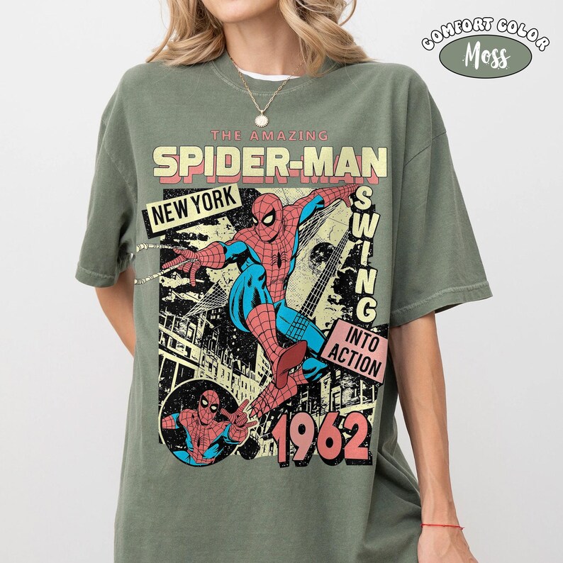 Peut inclure: Un t-shirt vert mousse avec un graphisme de Spider-Man se balan&ccedil;ant &agrave; New York. Le design comprend "THE AMAZING SPIDER-MAN", "NEW YORK", "SWING INTO ACTION" et l'ann&eacute;e "1962". Le t-shirt est &eacute;tiquet&eacute; "COMFORT COLOR Moss".