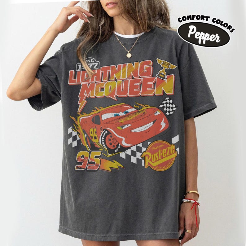 May include: Dark grey Lightning McQueen graphic t-shirt. The design features a red race car with the number 95, flames, and the text "Lightning McQueen" in red and yellow. The shirt also has the text "Rusteze" and a checkered flag.