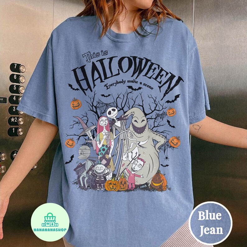 May include: Blue jean-colored t-shirt featuring a Halloween-themed graphic. The design includes characters, pumpkins, bats, and the text "This is Halloween, Everybody make a scene." The shirt is a comfortable, casual style.