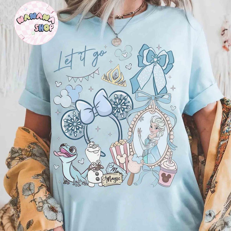 Może przedstawiać: Jasnoniebieska koszulka z nadrukiem z napisem "Let it go" i r&oacute;żnymi ilustracjami. Projekt zawiera portret księżniczki, płatki śniegu i postacie z kresk&oacute;wek. Koszulka ma podwinięte rękawy.