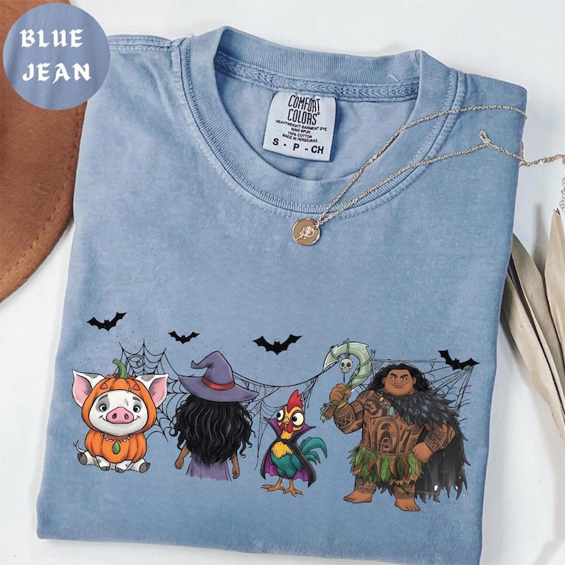 May include: Blue jean Comfort Colors t-shirt featuring a Halloween-themed graphic with cartoon characters. The design includes a pig in a pumpkin costume, a witch, a rooster, and a warrior. The shirt also has a Comfort Colors tag.