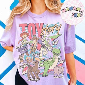 Puede incluir: Camiseta lila claro con dise&ntilde;o retro de "Toy Story", con personajes de dibujos animados como Jessie, Woody, Buzz, Rex, Hamm, Slinkydog y Bullseye. La camiseta tiene un aspecto vintage y desgastado.