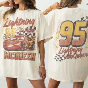 Puede incluir: Camiseta color crema con un gr&aacute;fico de Rayo McQueen de la pel&iacute;cula Cars. La parte delantera muestra el personaje con el texto "Lightning 95 McQueen". La parte trasera tiene un gran "95" con llamas y el texto "Lightning McQueen".