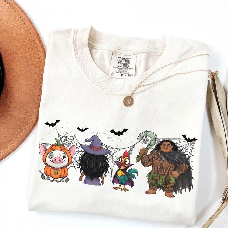 May include: Cream-colored Comfort Colors t-shirt featuring a Halloween-themed graphic. The design includes cartoon characters of a pig in a pumpkin, a witch, a rooster, and a Polynesian demigod. Black bats and spiderwebs complete the design.