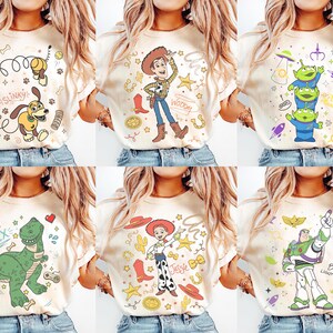 K&ouml;nnte beinhalten: Sechs cremefarbene T-Shirts, jedes mit einem anderen Cartoon-Charakter-Design. Designs umfassen Slinky Dog, Woody, drei gr&uuml;ne Aliens, Rex den Dinosaurier, Jessie und Buzz Lightyear.