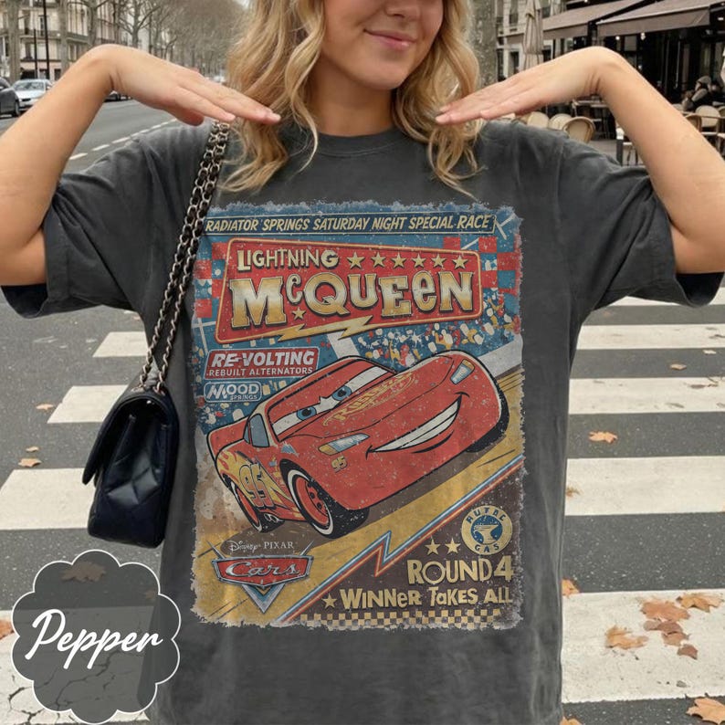 May include: Dark gray t-shirt featuring a graphic of Lightning McQueen from the Disney Pixar Cars movie. The design includes the text "RADIATOR SPRINGS SATURDAY NIGHT SPECIAL RACE" and "ROUND 4 WINNER TAKES ALL".