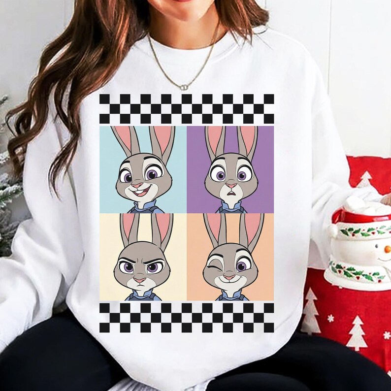 May include: White sweatshirt with a four-panel graphic of a cartoon rabbit with different facial expressions. The design is framed by a black and white checkered pattern. The rabbit is wearing a blue uniform.