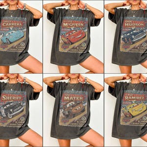 May include: Six dark gray t-shirts featuring different characters from the movie Cars. Each shirt has a vintage-style graphic with the character's name and a racing theme. The characters include Sally Carrera, Lightning McQueen, Doc Hudson, Sheriff, Tow Mater, and Cruz Ramirez.