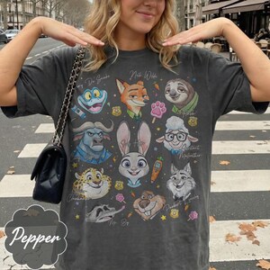 Pu&ograve; includere: T-shirt grigio scuro con personaggi dei cartoni animati di Zootropolis. La maglietta presenta immagini di Judy Hopps, Nick Wilde, Flash e altri personaggi. La parola "Pepper" &egrave; stampata in basso a sinistra.
