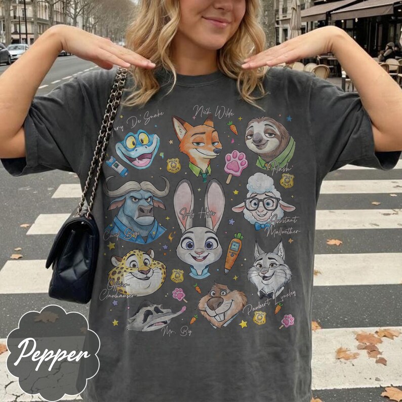 Pu&ograve; includere: T-shirt grigio scuro con personaggi dei cartoni animati di Zootropolis. La maglietta presenta immagini di Judy Hopps, Nick Wilde, Flash e altri personaggi. La parola "Pepper" &egrave; stampata in basso a sinistra.
