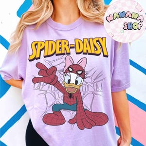 May include: A light purple t-shirt featuring a cartoon illustration of Daisy Duck as Spider-Man, with the text "SPIDER-DAISY" in yellow. The design includes a web background and the character in a Spider-Man costume.