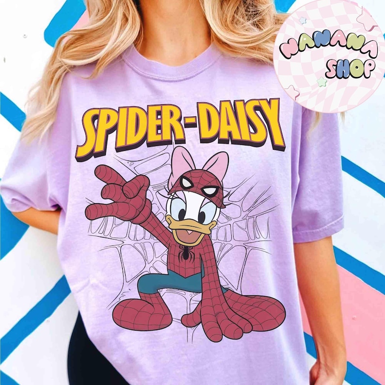 May include: A light purple t-shirt featuring a cartoon illustration of Daisy Duck as Spider-Man, with the text "SPIDER-DAISY" in yellow. The design includes a web background and the character in a Spider-Man costume.
