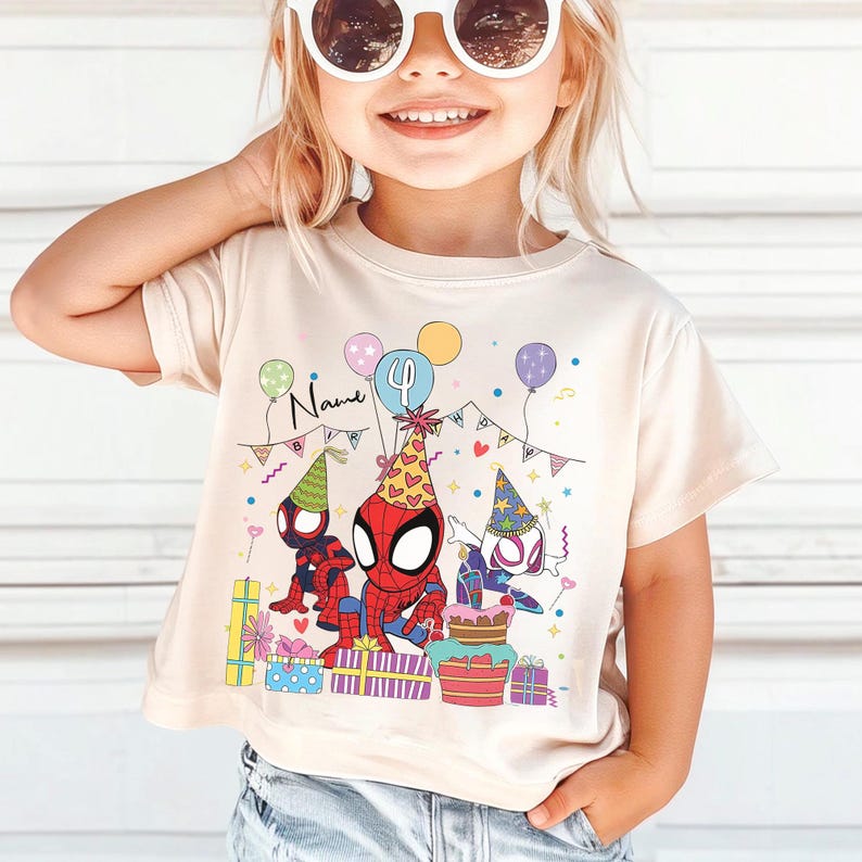 Pode incluir: Uma camiseta bege com um gr&aacute;fico colorido de personagens do Homem-Aranha celebrando um anivers&aacute;rio. O design inclui bal&otilde;es, presentes e um bolo. O n&uacute;mero 4 &eacute; exibido em um bal&atilde;o, e a palavra "Name" est&aacute; escrita acima dos personagens.
