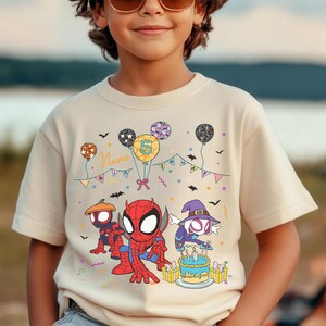 May include: Beige t-shirt featuring Spider-Man and other characters, balloons, and a birthday cake. The number 5 is on a balloon. The shirt has the word "Name" on it. The design is in red, blue, orange, purple, and yellow.