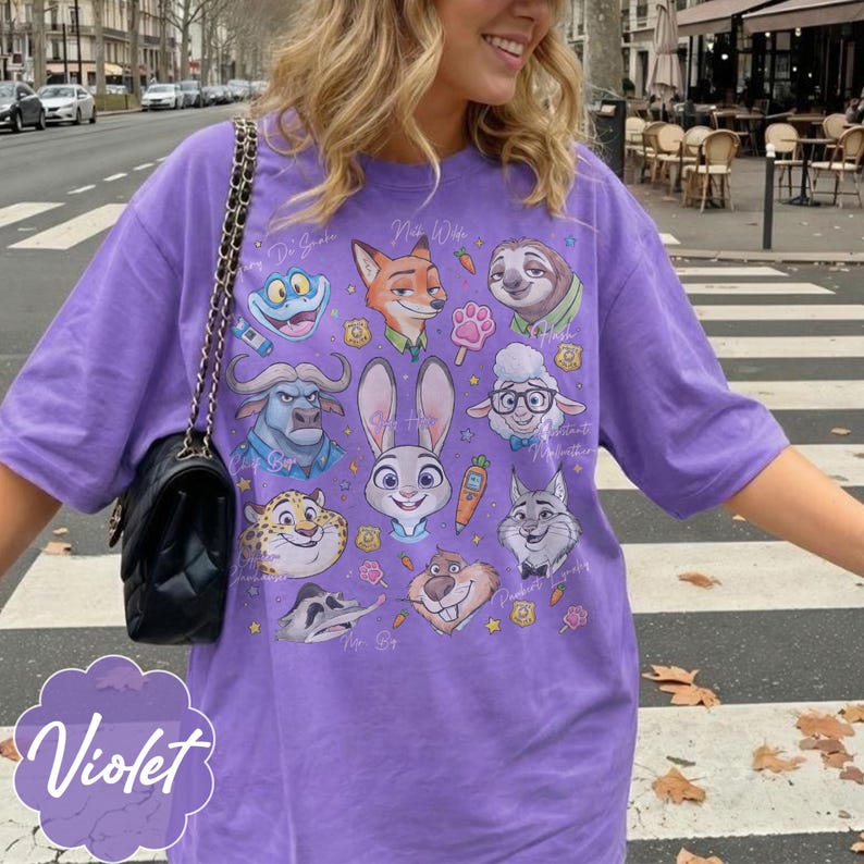 Pu&ograve; includere: T-shirt viola con grafica di personaggi di cartoni animati. La maglietta ha girocollo e maniche corte. La parola "Violet" &egrave; stampata in corsivo in basso a sinistra.