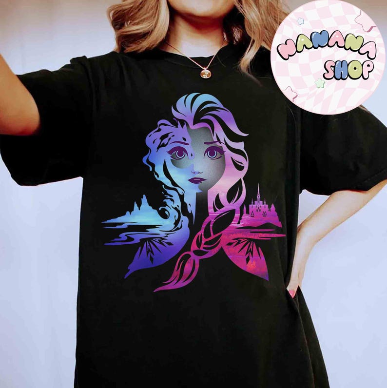 May include: Black t-shirt featuring a colorful graphic of a woman's face split into two halves, with a castle and landscape design. The design incorporates shades of blue, purple, and pink. A circular logo with the text "NANANA SHOP" is in the upper right corner.