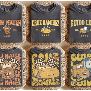 May include: Six charcoal grey t-shirts featuring designs from the Cars movie. Each shirt displays a character's name in a vintage font, along with the text "EST. 2006 CARS" and a cartoon image of the character. The designs include Tow Mater, Cruz Ramirez, and Guido Luigi.
