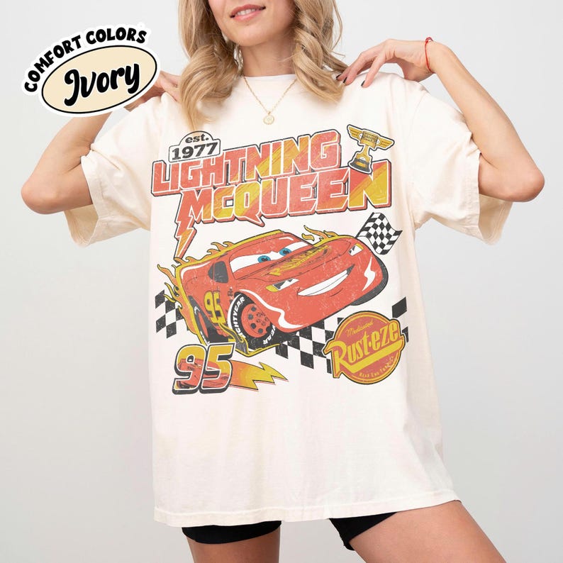 May include: Ivory t-shirt with a Lightning McQueen graphic from the film Cars. The design includes the text "Lightning McQueen" and "95", a checkered flag, and the "Rust-eze" logo. The shirt has a vintage, distressed appearance.