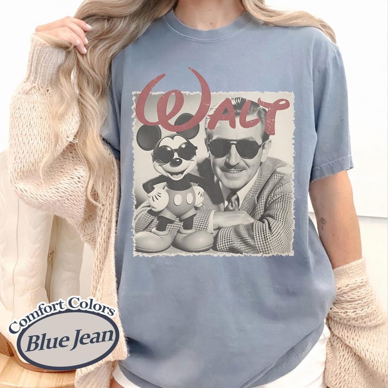 Pu&ograve; includere: T-shirt blu chiaro a maniche corte con una grafica di Topolino e Walt Disney con occhiali da sole. La parola "WALT" &egrave; stampata sopra l'immagine in rosso. La maglietta &egrave; etichettata "Comfort Colors Blue Jean".