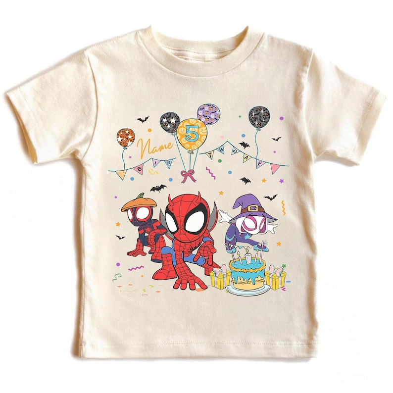 May include: Cream-colored t-shirt featuring cartoon Spider-Man characters. The design includes balloons, a birthday cake, and the number 5. The word "Name" is also visible. The shirt is decorated with bats and colorful confetti.