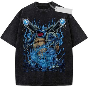 May include: A black acid-wash short-sleeve t-shirt featuring a graphic illustration of a blue turtle-like creature with two large cannons on its back, surrounded by swirling blue flames and water effects, with a blank white rectangular price tag attached.