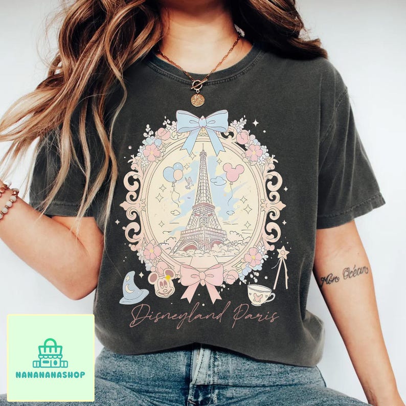 Peut inclure: T-shirt gris fonc&eacute; avec un motif Disneyland Paris. Le graphisme comprend la Tour Eiffel, Mickey Mouse et des n&oelig;uds d&eacute;coratifs. Les mots "Disneyland Paris" sont &eacute;crits en &eacute;criture cursive.