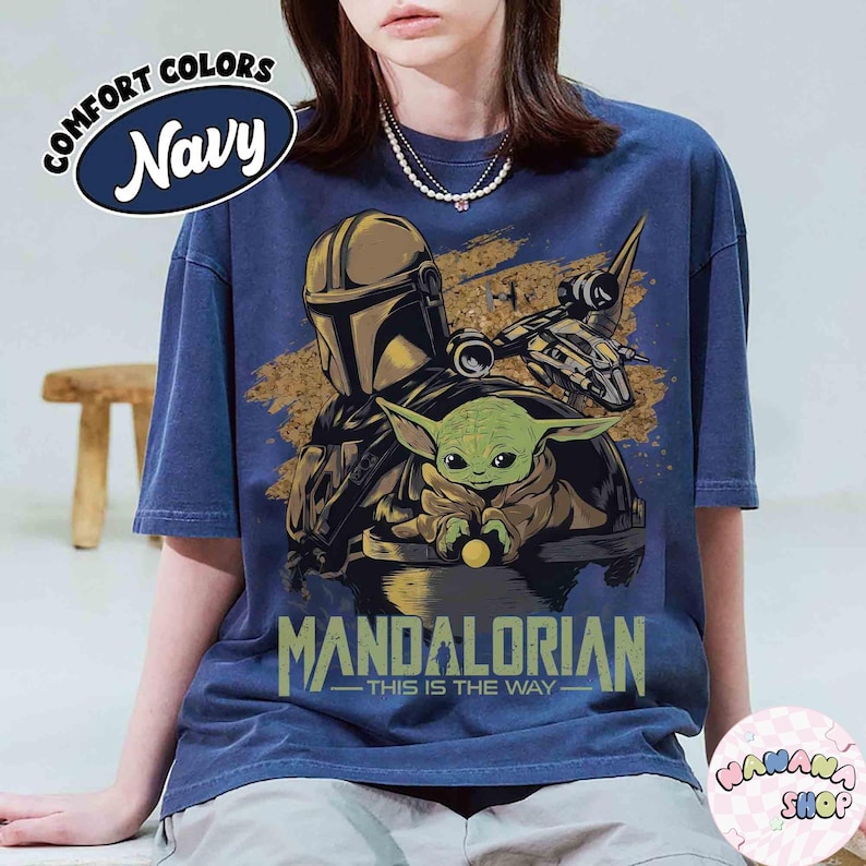 Puede incluir: Camiseta azul marino con un dise&ntilde;o de The Mandalorian y Grogu, con el texto "MANDALORIAN - THIS IS THE WAY". La camiseta tambi&eacute;n tiene el texto "COMFORT COLORS Navy" en un c&iacute;rculo. La camiseta es de corte holgado.