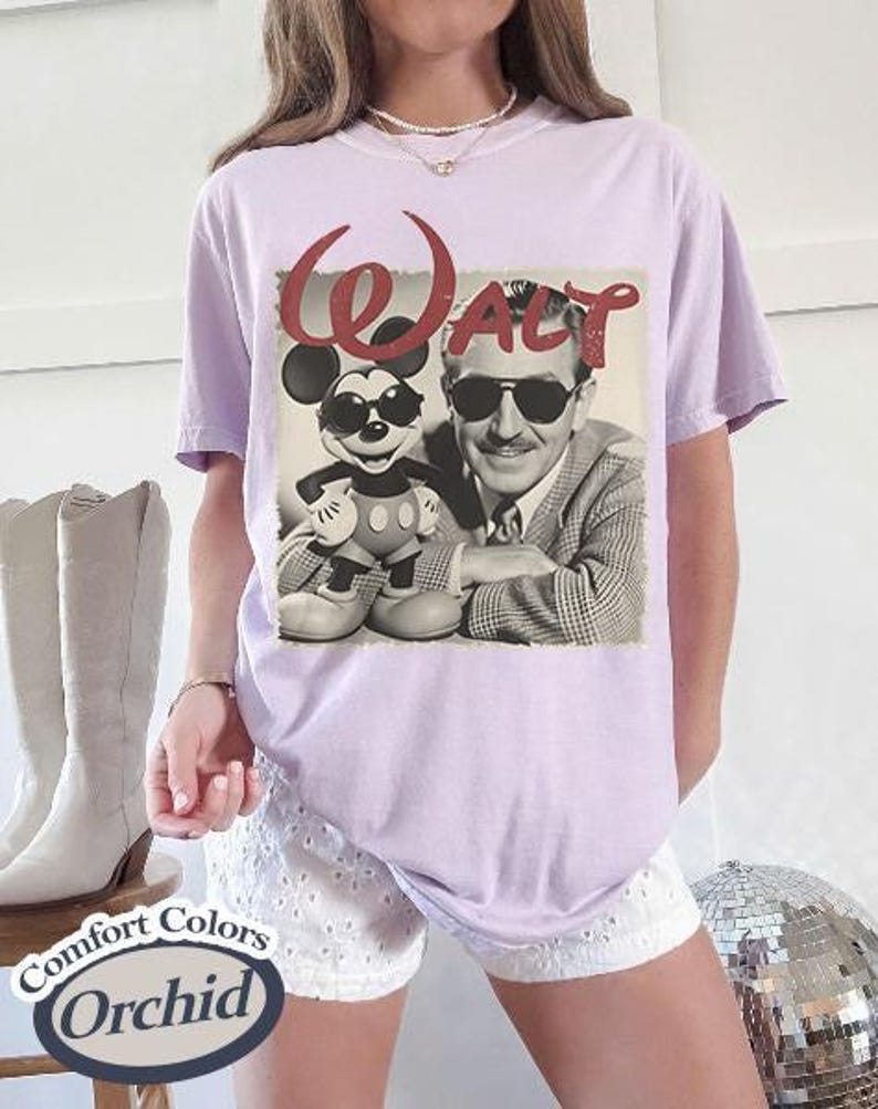 Pu&ograve; includere: Una maglietta lilla Comfort Colors con un'immagine in bianco e nero di Walt Disney e Mickey Mouse con occhiali da sole. La parola "Walt" &egrave; in corsivo rosso sopra l'immagine. La maglietta ha una vestibilit&agrave; rilassata.