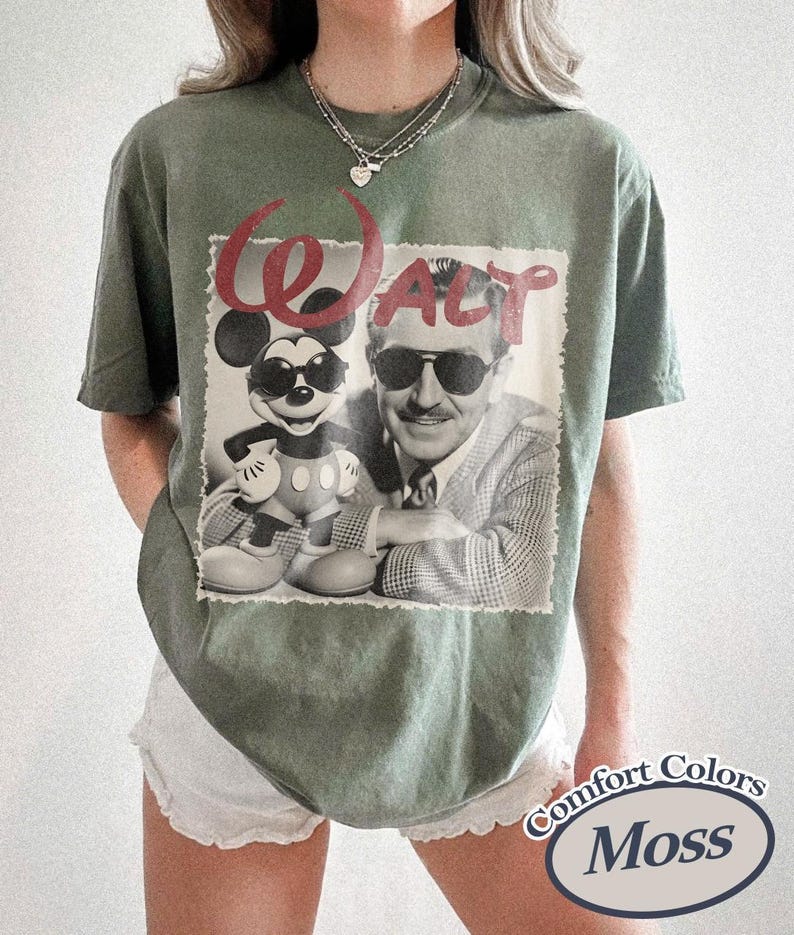 Pu&ograve; includere: T-shirt verde muschio con un'immagine in bianco e nero di Topolino e Walt Disney. La parola "WALT" &egrave; in corsivo rosso sopra l'immagine. La maglietta ha un aspetto vintage e le parole "Comfort Colors Moss" sono stampate in basso a destra.