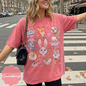 Pu&ograve; includere: Una maglietta color corallo con personaggi dei cartoni animati di Zootopia. La maglietta ha un girocollo e maniche corte. I personaggi includono Judy Hopps, Nick Wilde e Flash. Il testo "Crunchberry" &egrave; in basso.