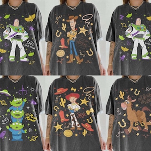 K&ouml;nnte beinhalten: Sechs dunkelgraue T-Shirts mit Toy Story-Charakteren. Designs umfassen Buzz Lightyear, Woody, Jessie und die Aliens von Pizza Planet. Jedes Shirt hat eine einzigartige Grafik mit dem Namen der Figur oder zugeh&ouml;rigem Text.