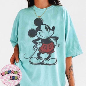 K&ouml;nnte beinhalten: Hellblaues T-Shirt mit einer skizzenhaften Illustration von Mickey Mouse. Die Zeichentrickfigur ist in Schwarz, Rot und Wei&szlig; dargestellt. Das T-Shirt hat eine lockere Passform und kurze &Auml;rmel.