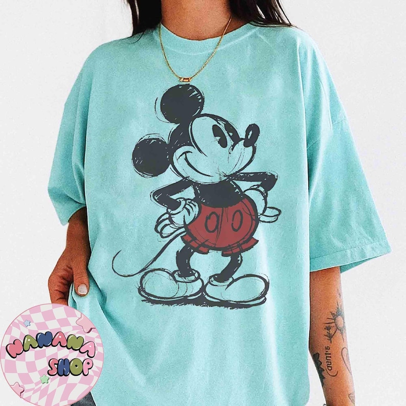 K&ouml;nnte beinhalten: Hellblaues T-Shirt mit einer skizzenhaften Illustration von Mickey Mouse. Die Zeichentrickfigur ist in Schwarz, Rot und Wei&szlig; dargestellt. Das T-Shirt hat eine lockere Passform und kurze &Auml;rmel.
