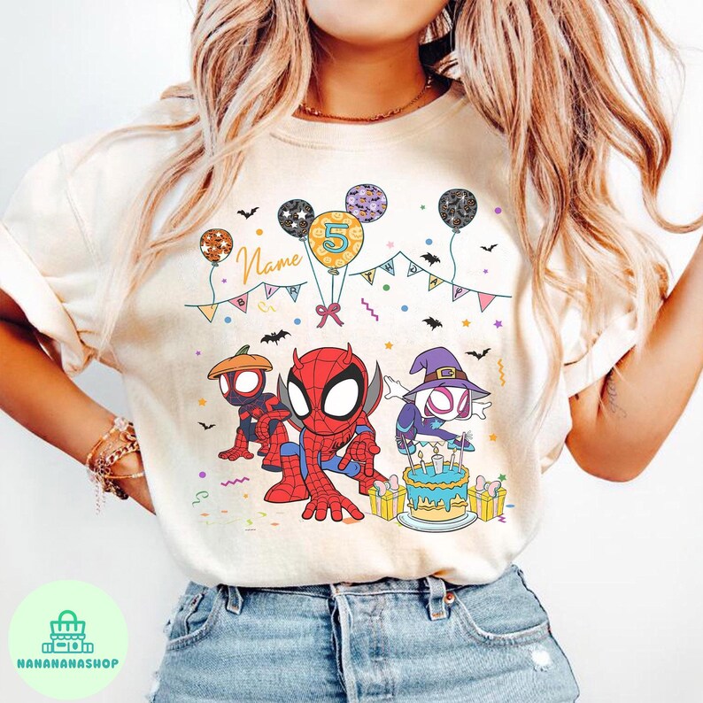 May include: Cream-colored t-shirt featuring a colorful birthday design with Spider-Man characters. The design includes balloons, a cake, and the number 5. The word "Name" is also visible. The shirt is worn by a person.