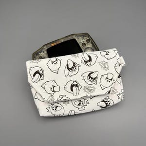 May include: A white pouch featuring a repeating black line art pattern of Boo characters with tongues sticking out and the word Boo in speech bubbles. A translucent grey handheld gaming console is partially tucked inside the pouch.