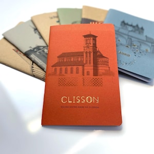 May include: A collection of notebooks featuring architectural designs. The front notebook is a burnt orange colour, displaying a church illustration and the word "Clisson" in gold. The text "Eglise Notre-Dame de Clisson" is below. Other notebooks have similar designs.