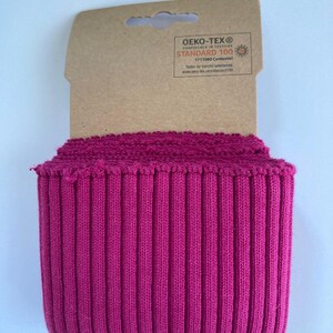 May include: A roll of vibrant fuchsia ribbed knit fabric. The fabric is tightly woven with vertical ridges, and is attached to a cardboard tag with the "OEKO-TEX&reg; STANDARD 100" label.