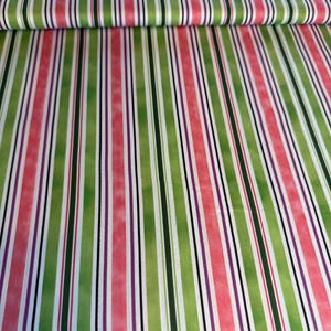 Puede incluir: Tela con un patrón de rayas verticales en tonos verdes, rosas, morados, negros y blancos. La tela está doblada, mostrando el patrón repetido. Las rayas son de diferentes anchos, creando un diseño visualmente interesante.