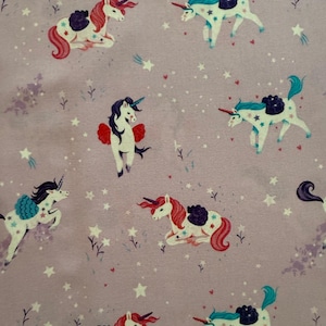 Könnte beinhalten: Ein helllila Stoff mit einem sich wiederholenden Muster aus Einhörnern und Sternen. Die Einhörner haben bunte Mähnen und Schweife, einige sitzen, andere tanzen. Weiße Sterne sind über den Hintergrund verstreut.