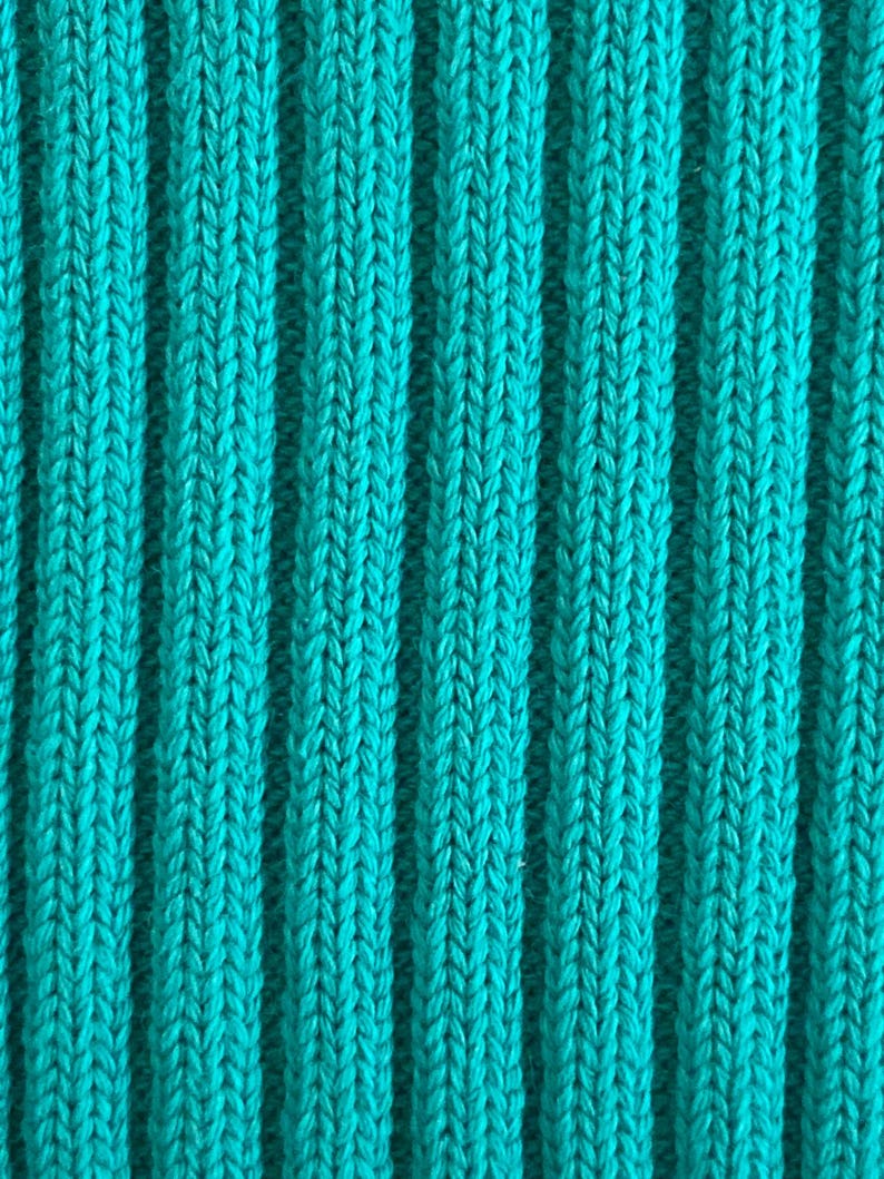May include: Close-up of a teal ribbed knit fabric. The fabric has vertical ridges and a textured surface. The color is a vibrant, solid teal, with a slight sheen. The knit pattern is visible, creating a visually interesting texture.