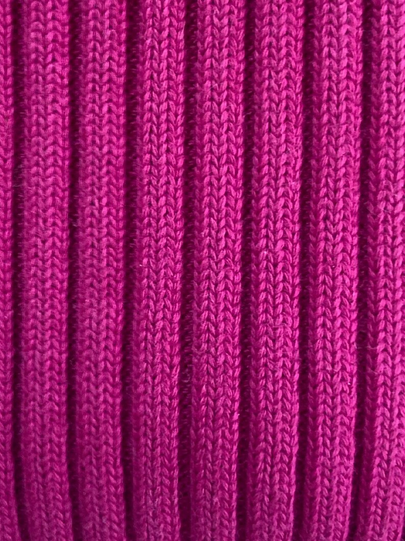 May include: Close-up of a vibrant magenta ribbed knit fabric. The vertical ribs create a textured pattern, showcasing the detailed knit structure. The color is a rich, saturated hue, suggesting a warm and cozy textile, possibly for clothing or home decor.
