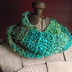 May include: A teal, green and brown crocheted infinity scarf on a grey dress form.