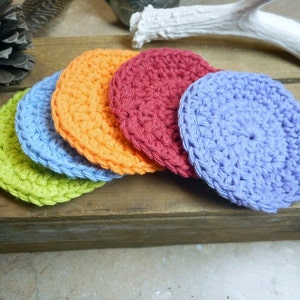 May include: Five crocheted coasters in different colors: green, blue, orange, red, and purple. The coasters are stacked on top of each other.