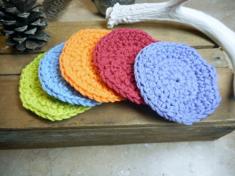May include: Five crocheted coasters in different colors: green, blue, orange, red, and purple. The coasters are stacked on top of each other.