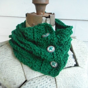 May include: A green crocheted cowl with three decorative buttons. The buttons have a white and green floral design.
