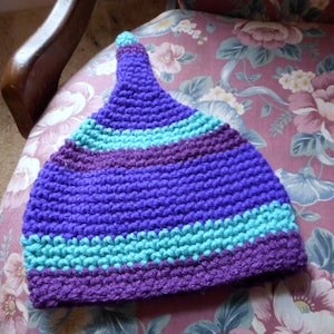May include: Purple and teal striped crocheted hat with a pointed top.