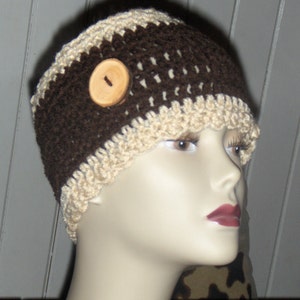 May include: A brown and beige crocheted headband with a wooden button. The headband is worn on a mannequin's head.