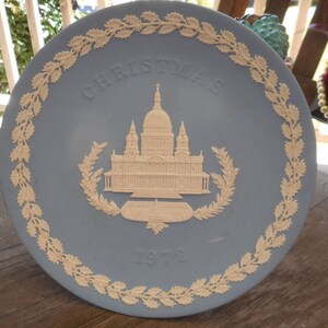 May include: A blue and white ceramic Christmas plate featuring a relief design of St. Paul's Cathedral in London. The plate has a white border with a holly leaf design and the text "Christmas 1972".