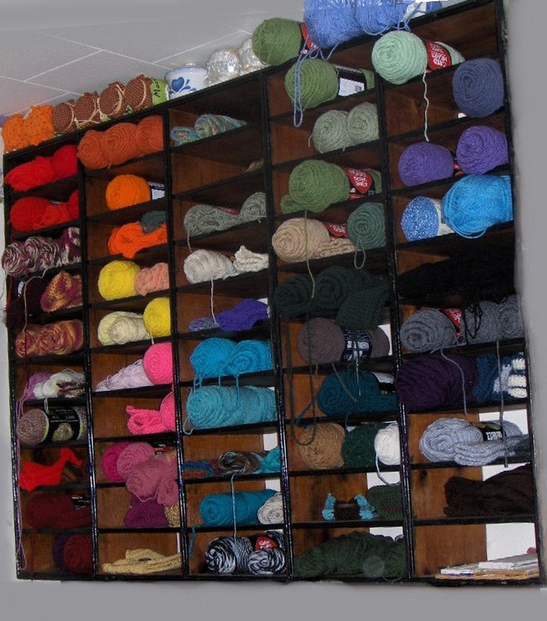 May include: A wooden shelf unit filled with various colors of yarn. The yarn is organized by color and is displayed in rows on the shelves.